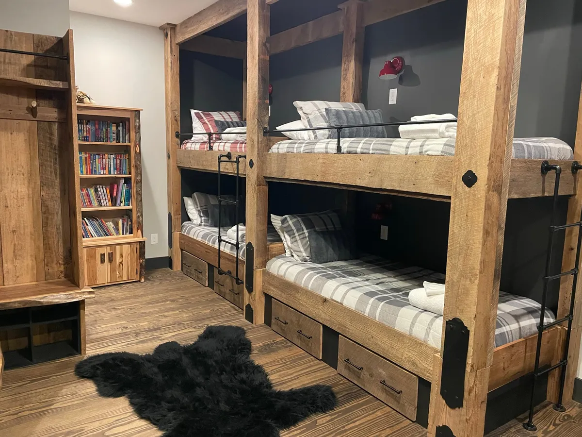 A playful lower-level bunk room equipped with multiple bunk beds, a bookshelf filled with books, and a cozy rug. The space is designed to encourage both sleep and storytelling, perfect for groups or families with children.