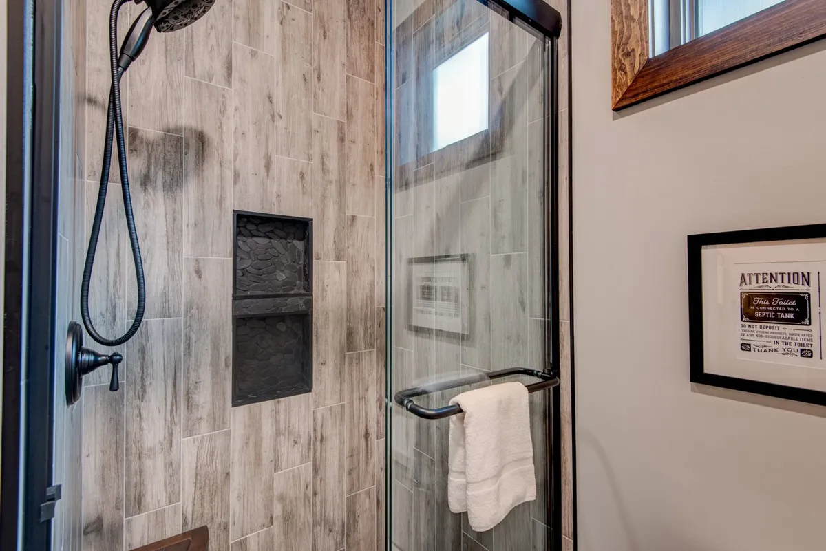 A modern, spa-inspired bathroom with a glass shower enclosure, textured wall tiles, and a towel neatly hanging on a rack. The design is clean and inviting, hinting at the luxury finishes like granite or quartz vanities.